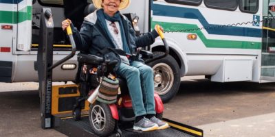 Smiling woman in a powerchair exiting a paratransit bus via electric lift