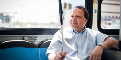Smiling man riding a bus with a white cane