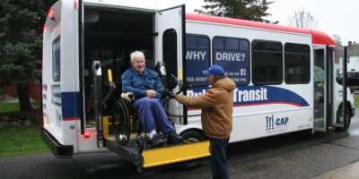 Driver assisting man on wheelchair on lift exiting the vehicle