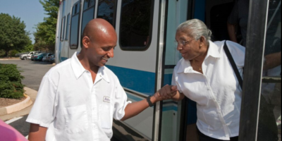Male bus driver extending hand to helpto help older woman off bus