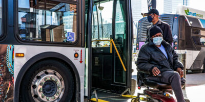 Driver assists passenger in power wheelchair using ramp to exit fixed-route bus