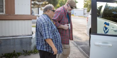Driver assisting man with vision impairment into a transit van