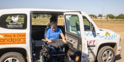 Young man in power wheelchair exiting volunteer transportation vehicle using ramp.