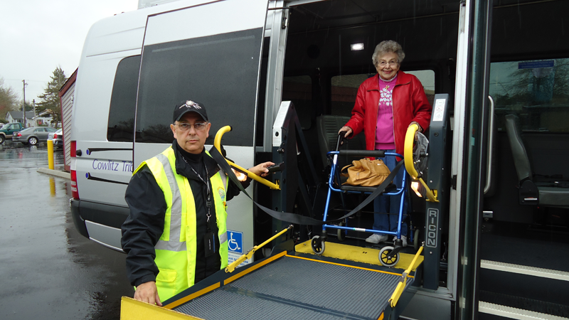 Photo of vehicle driver assisting an older woman with a walker using the vehicle's lift