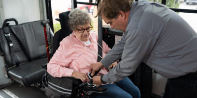 Driver securing passenger in electric wheelchair on bus