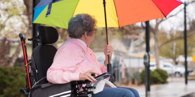 Older adult in electric wheelchair holding a colorful umbrella