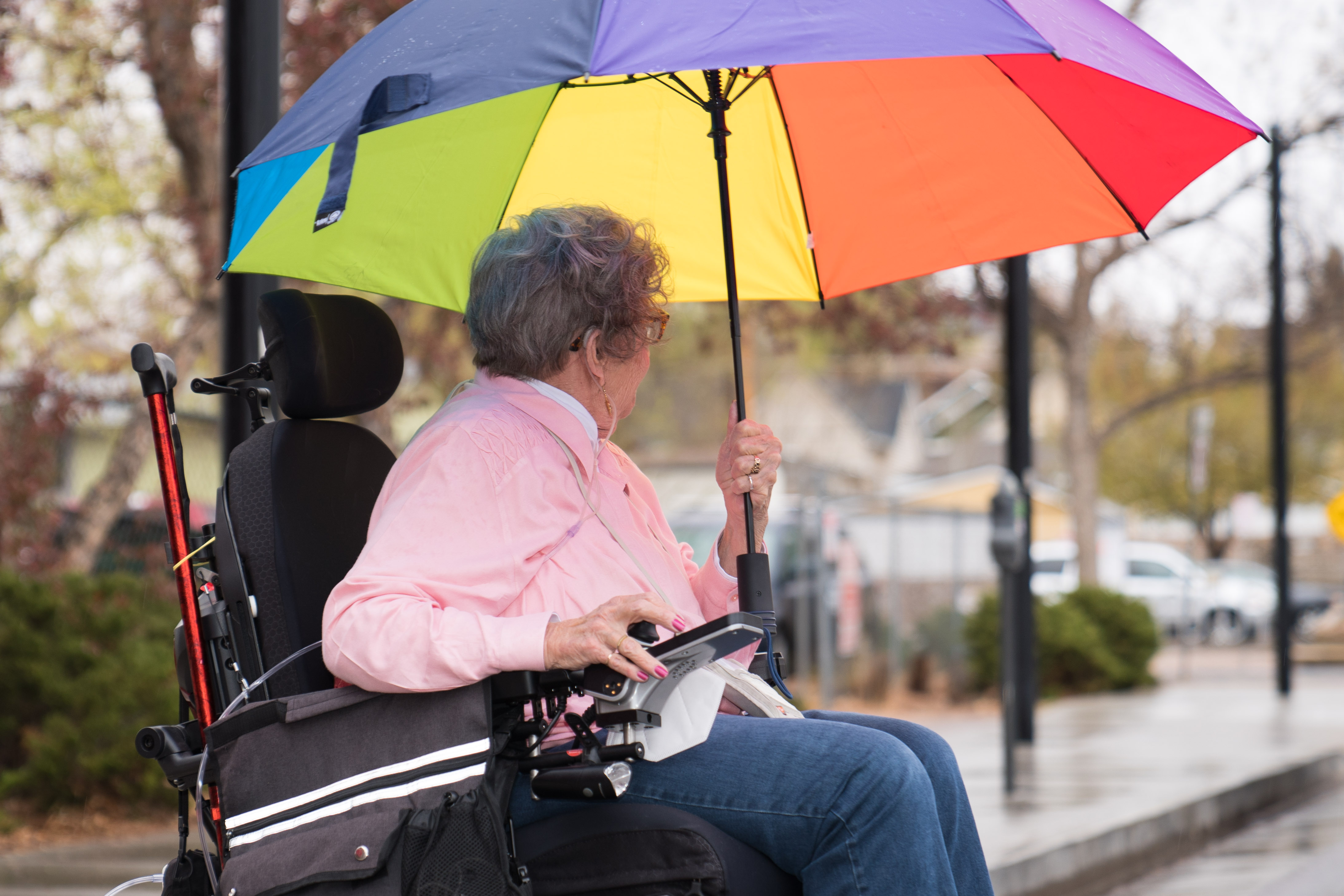 Older adult in electric wheelchair holding a colorful umbrella