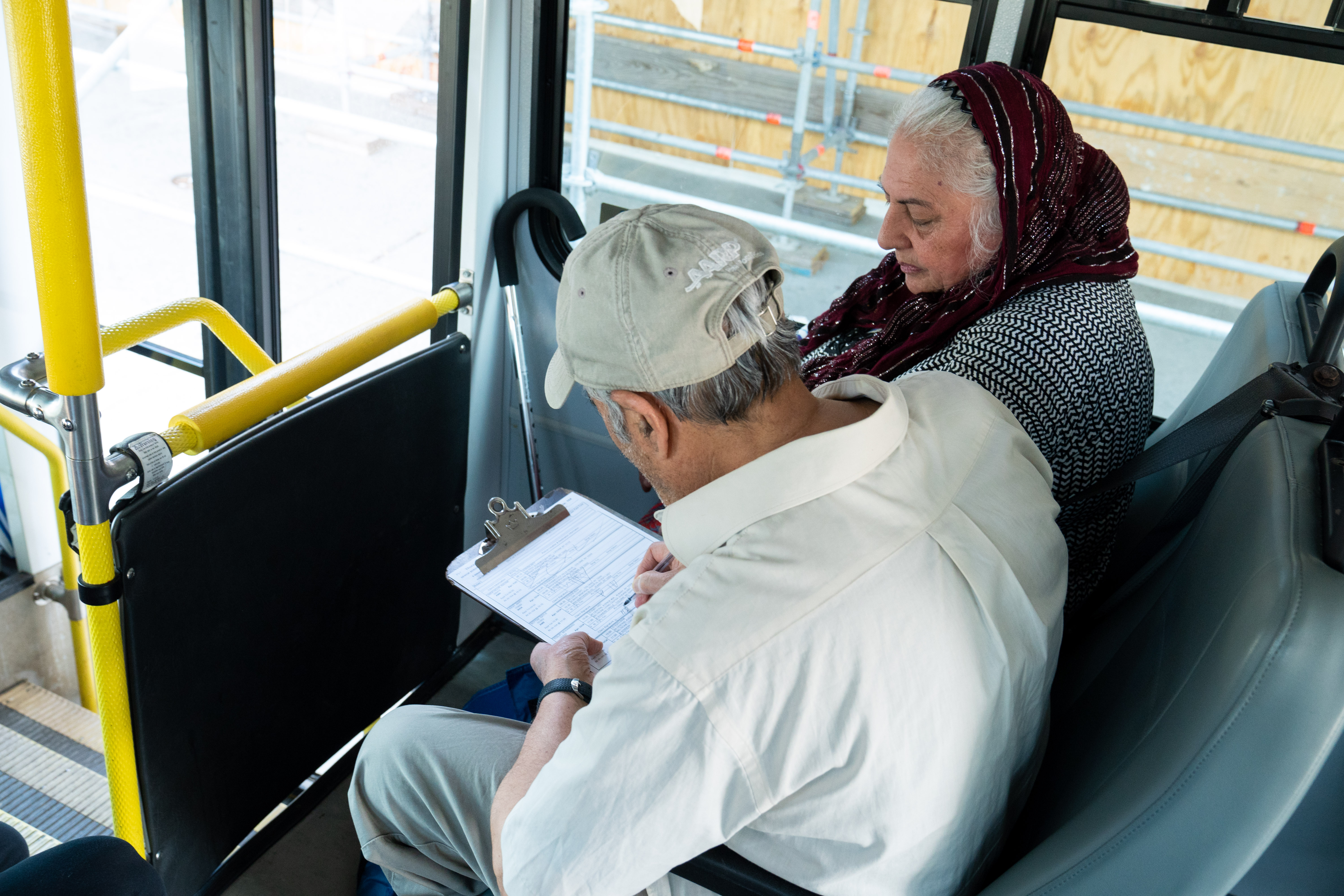 Couple seated on bus writing on clipboard 