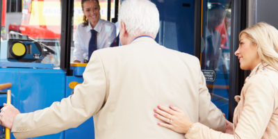 woman assisting older man onto a bus with bus driver smiling at them