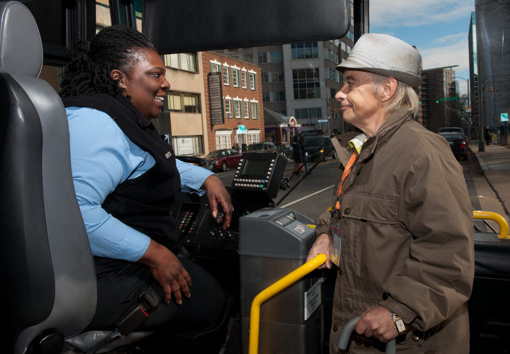 Photo of older man showing a transit fare pass to a bus driver.