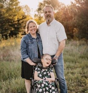 woman, man, and young girl in a wheelchair posing outdoors for family photo