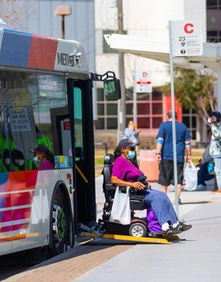 Woman in motorized wheelchair exits bus from ramp onto city sidewalk