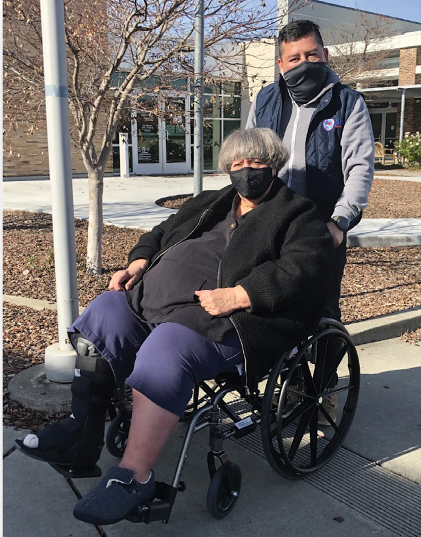 man pushing woman in wheelchair , both wearing masks