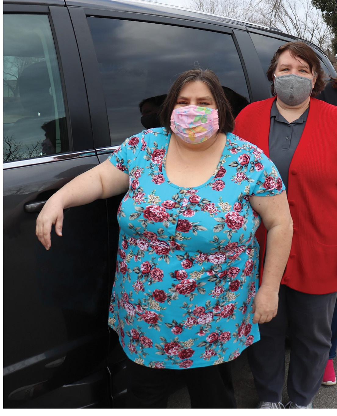 Two women wearing masks stand next to van