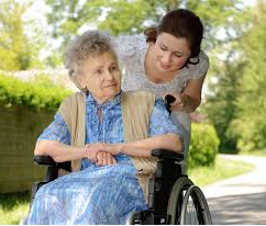 A Personal Care Attendant assists an older woman in a wheelchair.