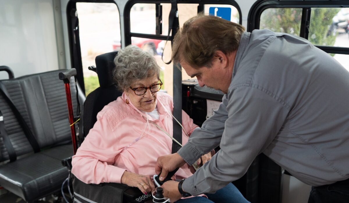 Driver helps secure older woman's wheelchair in van.