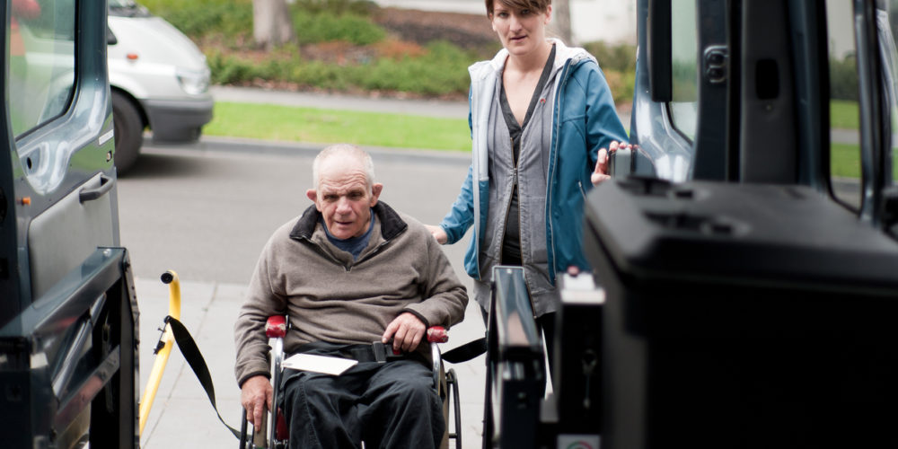 Man in wheelchair entering a modified van shot from inside the vehicle, and with a female support worker by his side.