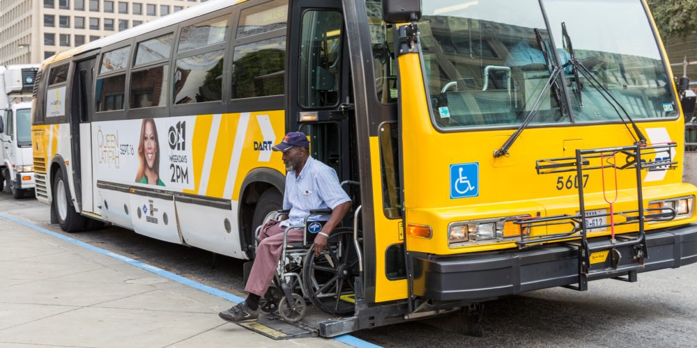 Man in wheelchair using ramp to deboard fixed-route bus in Dallas.