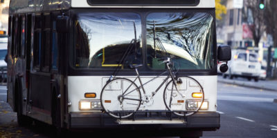 Large public bus with bike secured to front driving down city road