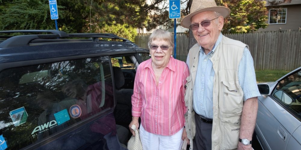 Older man and woman standing next to their car