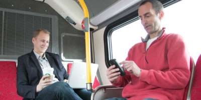 Two men looking at phone and laptop on bus Credit: OmniTrans San Bernardino